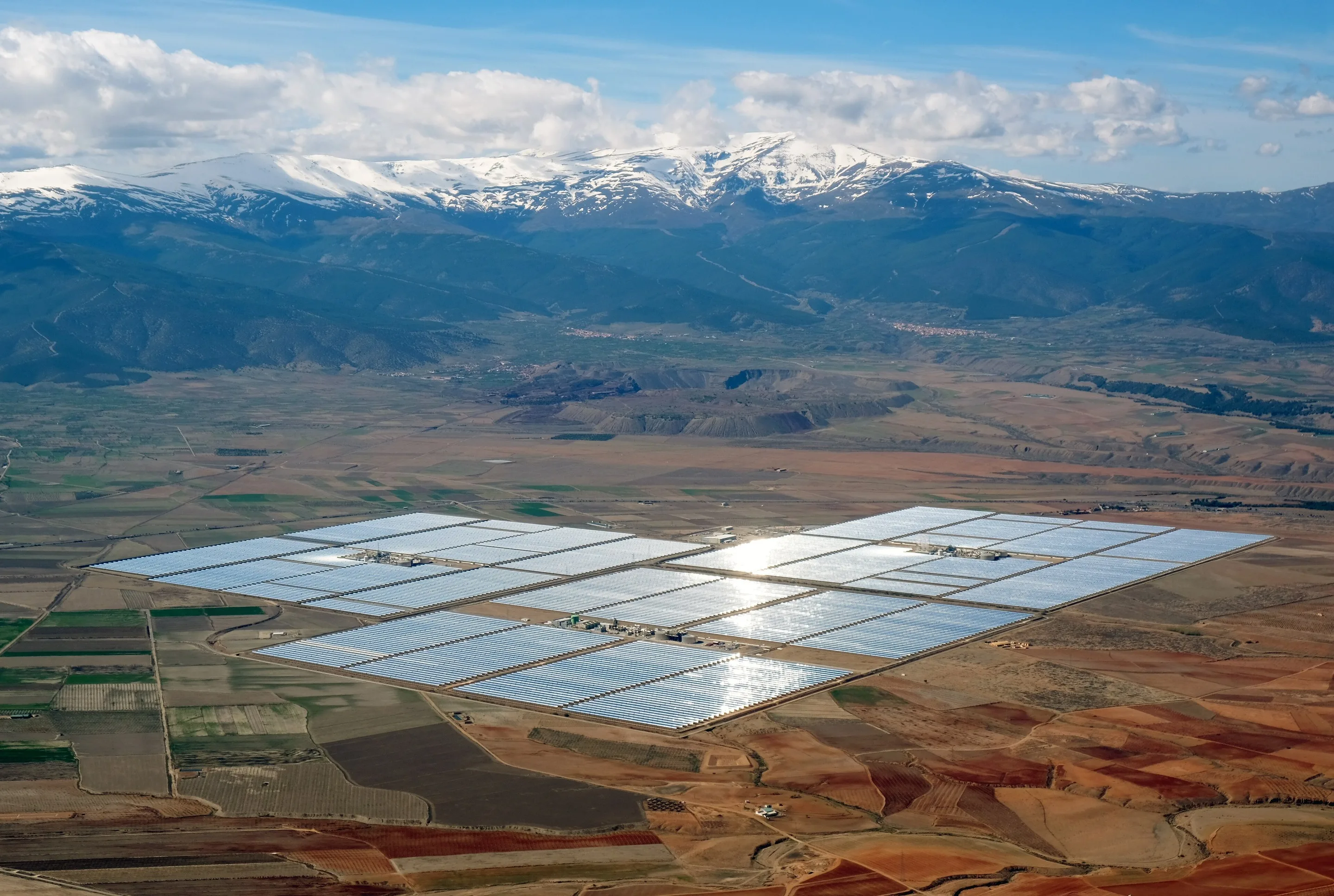 A vast solar power station on a plain beneath snow-capped mountains